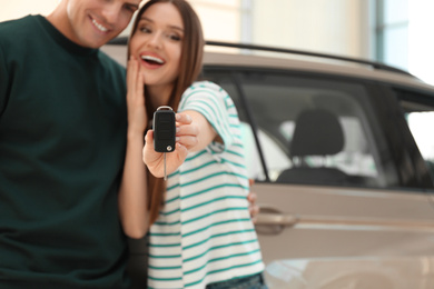 Photo of Happy couple with car key in modern auto dealership, focus on hand