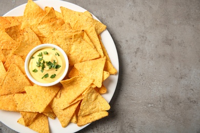 Photo of Plate with delicious mexican nachos chips and cheese sauce on grey table, top view. Space for text