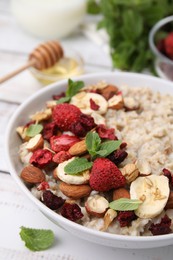 Photo of Delicious oatmeal with freeze dried berries, banana, nuts and mint on white table, closeup