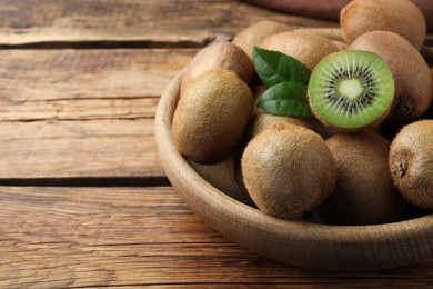Photo of Bowl with cut and whole fresh kiwis on wooden table, closeup. Space for text