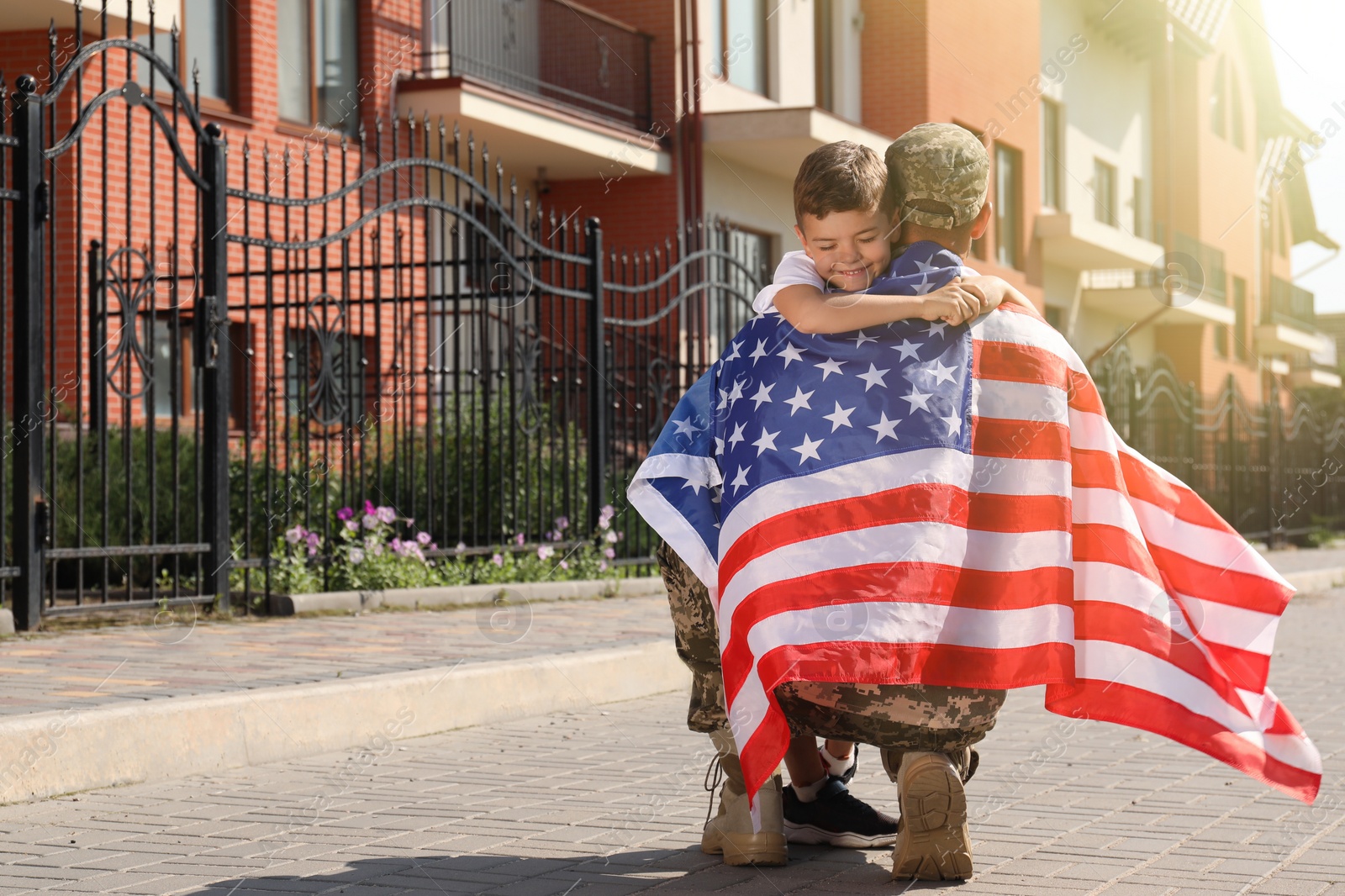 Photo of Soldier with flag of USA and his little son hugging outdoors