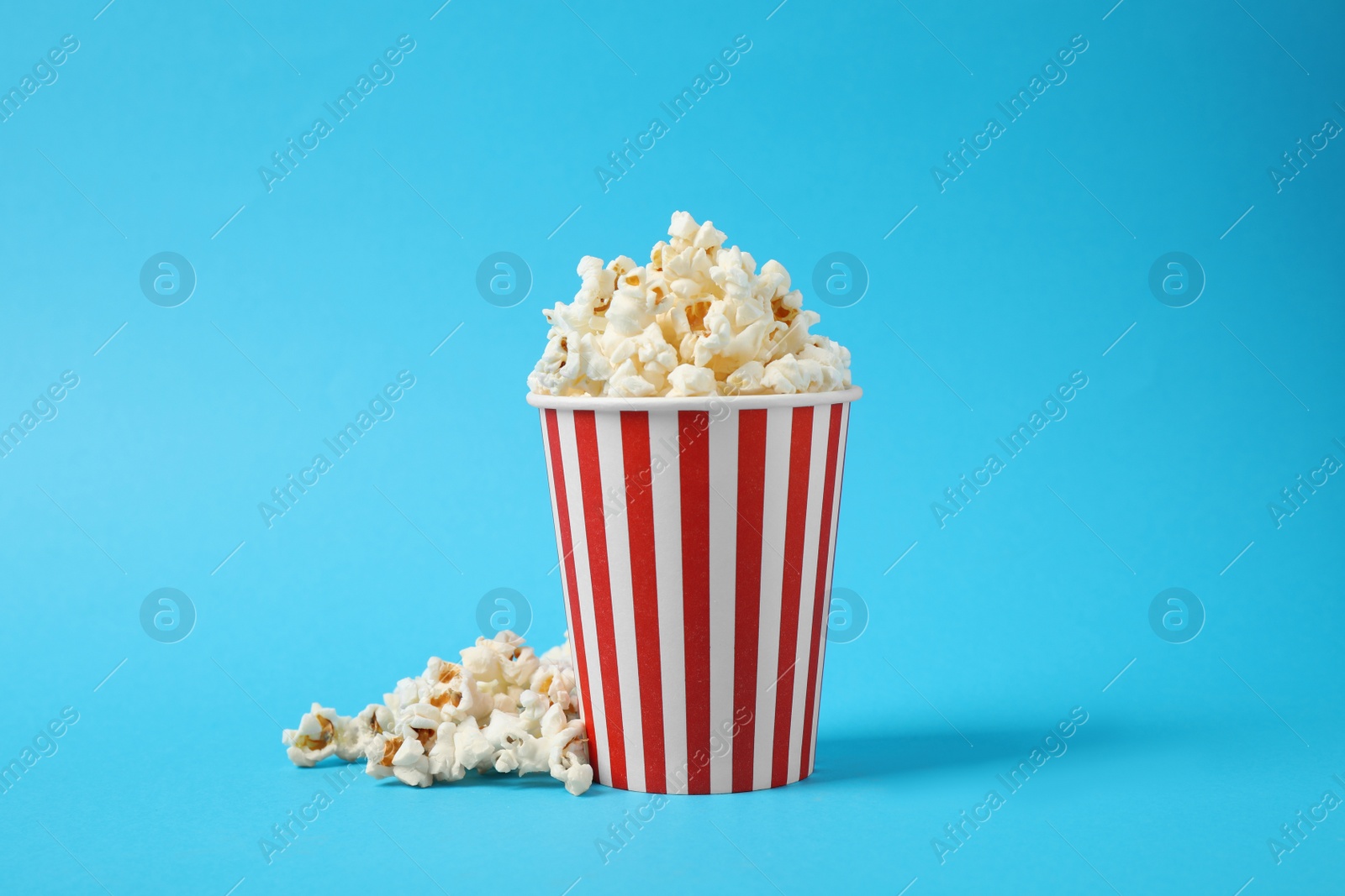 Photo of Delicious popcorn in paper cup on light blue background