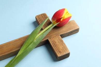 Easter - celebration of Jesus resurrection. Wooden cross and tulip on light blue background, closeup