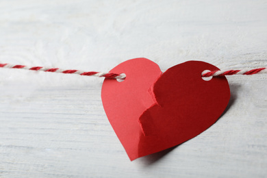 Photo of Broken red paper heart and rope on white wooden table, closeup. Relationship problems concept
