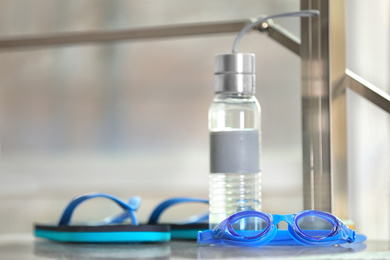 Photo of Swimming goggles, water bottle and flip flops against blurred background