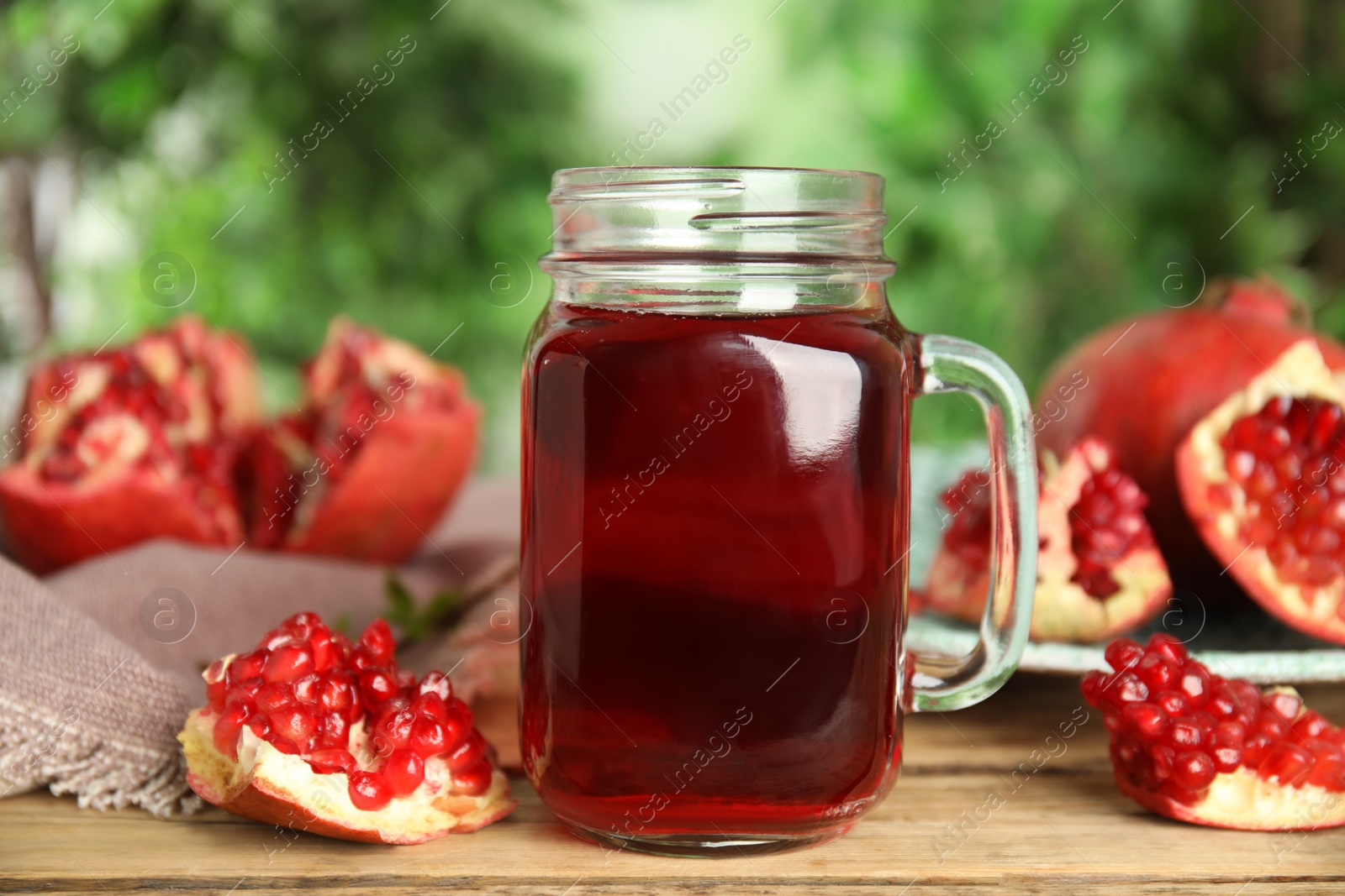 Photo of Pomegranate juice in mason jar and fresh fruits on wooden table outdoors