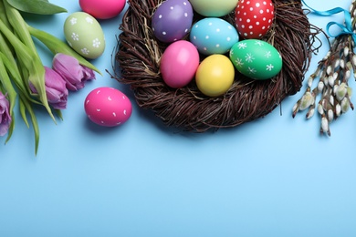 Photo of Flat lay composition with bright painted eggs on light blue background, space for text. Happy Easter