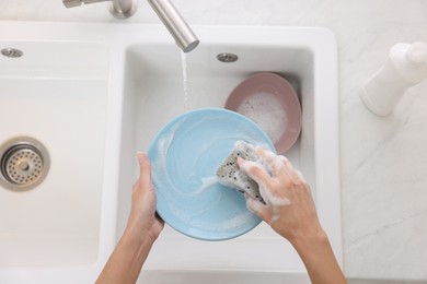 Photo of Woman washing plate above sink in modern kitchen, top view
