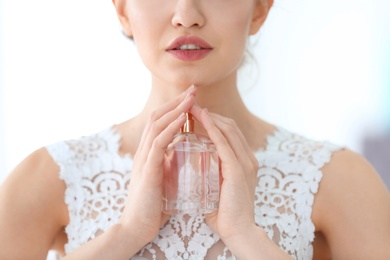 Photo of Beautiful young bride with bottle of perfume on light background, closeup