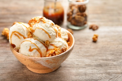 Photo of Tasty ice cream with caramel sauce and popcorn in bowl on wooden table