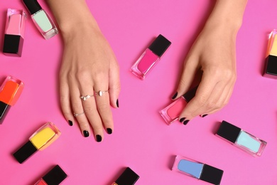 Woman with black manicure and nail polish bottles on color background, top view