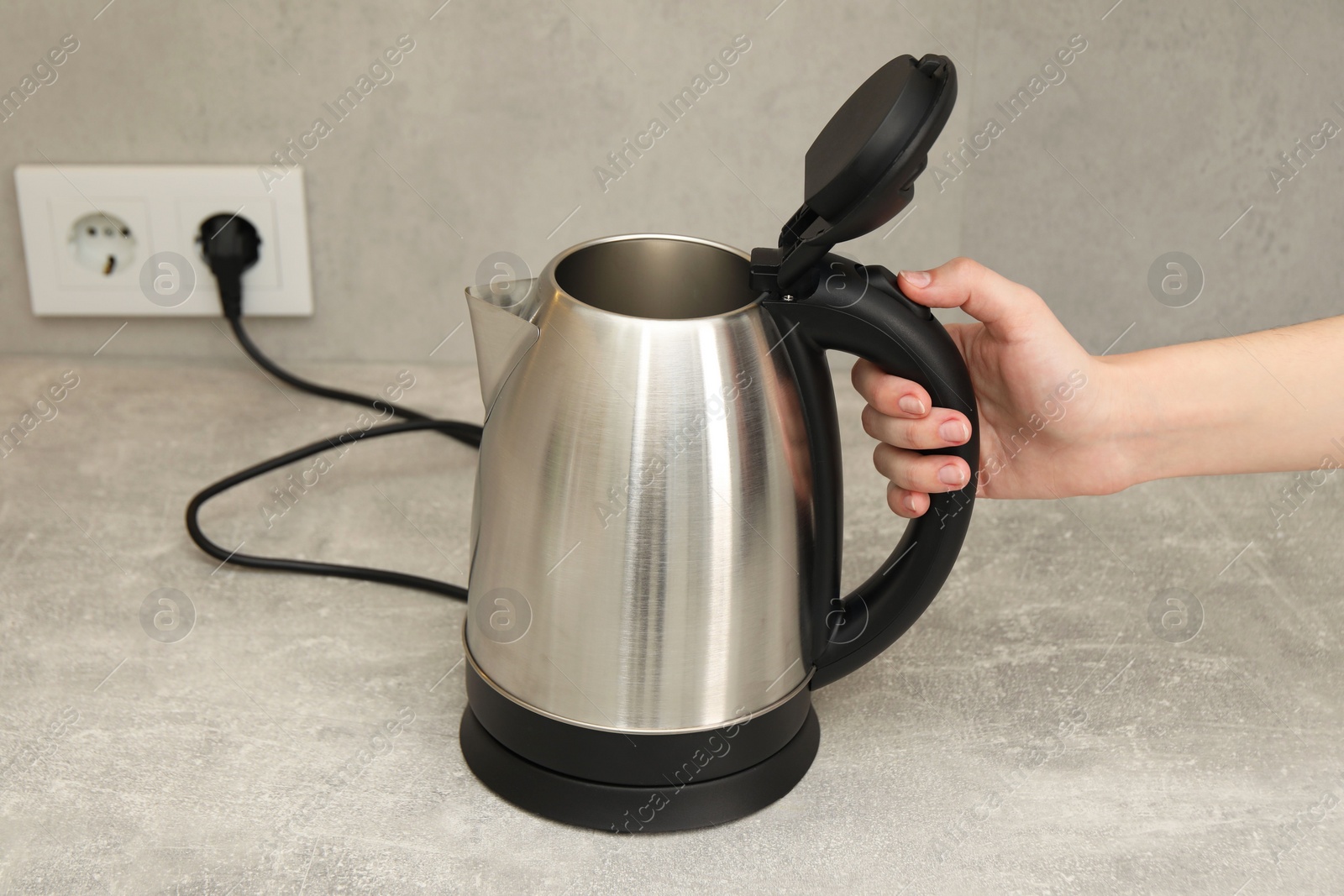 Photo of Woman with electric kettle in kitchen, closeup