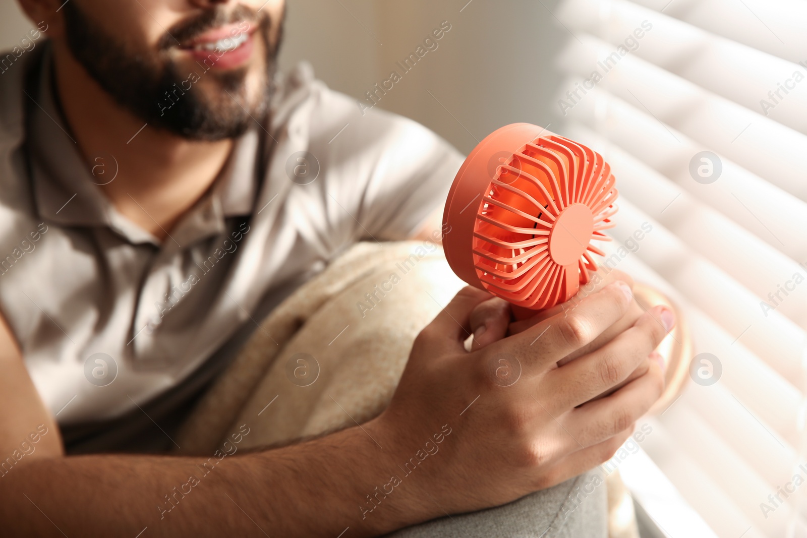 Photo of Man enjoying air flow from portable fan at home, closeup. Summer heat