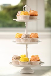 Photo of Dessert stand with tasty cupcakes on table indoors, closeup