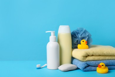 Photo of Baby cosmetic products, bath ducks, accessories and towels on light blue background. Space for text