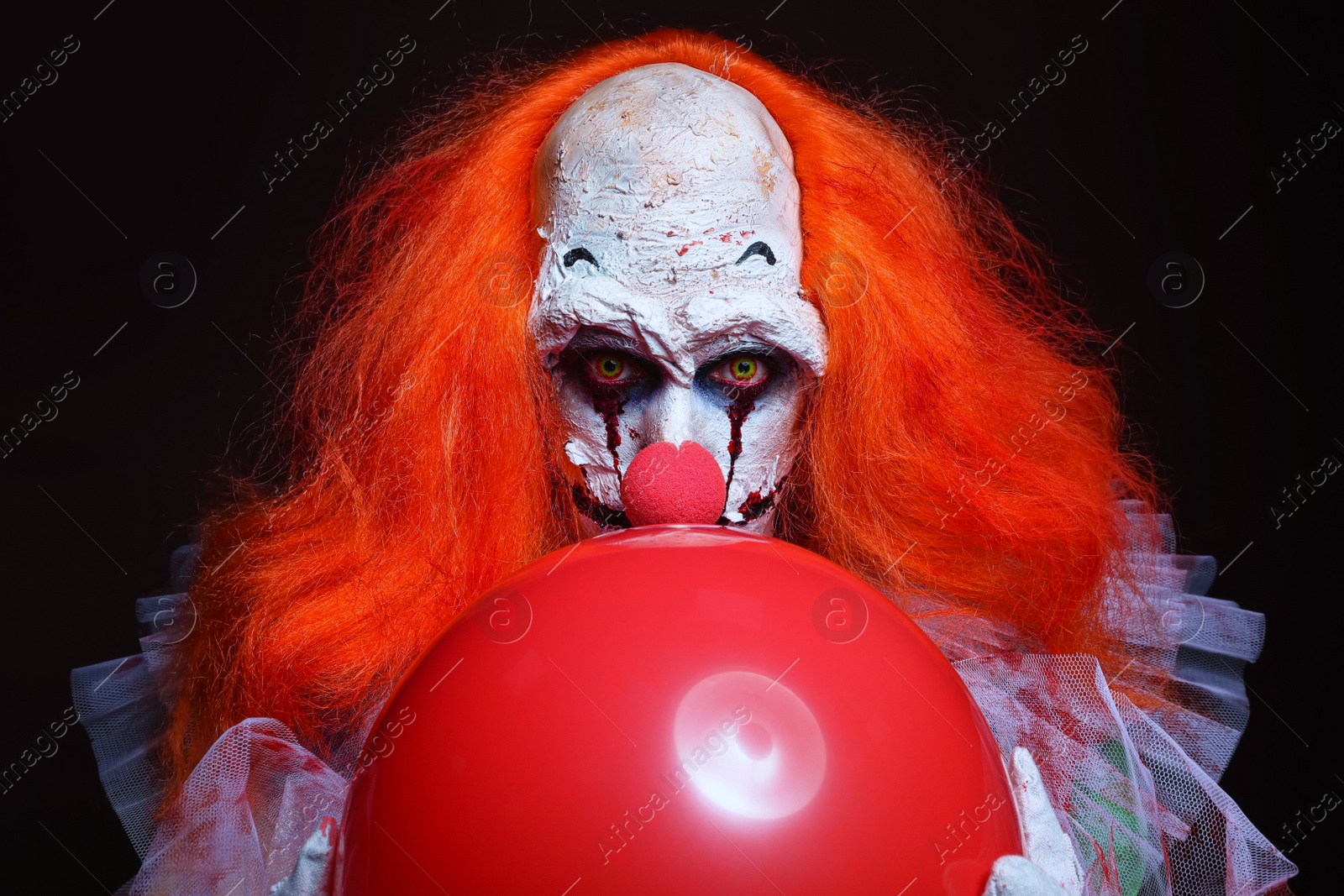 Photo of Terrifying clown with red air balloon on black background. Halloween party costume