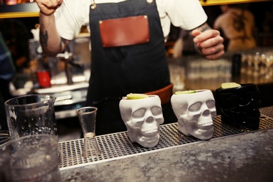 Photo of Bartender and skull cups of tasty cocktail on counter in nightclub, closeup