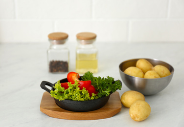 Photo of Raw potatoes and portioned frying pan with products on table