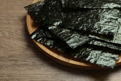 Photo of Plate with dry nori sheets on wooden table, closeup