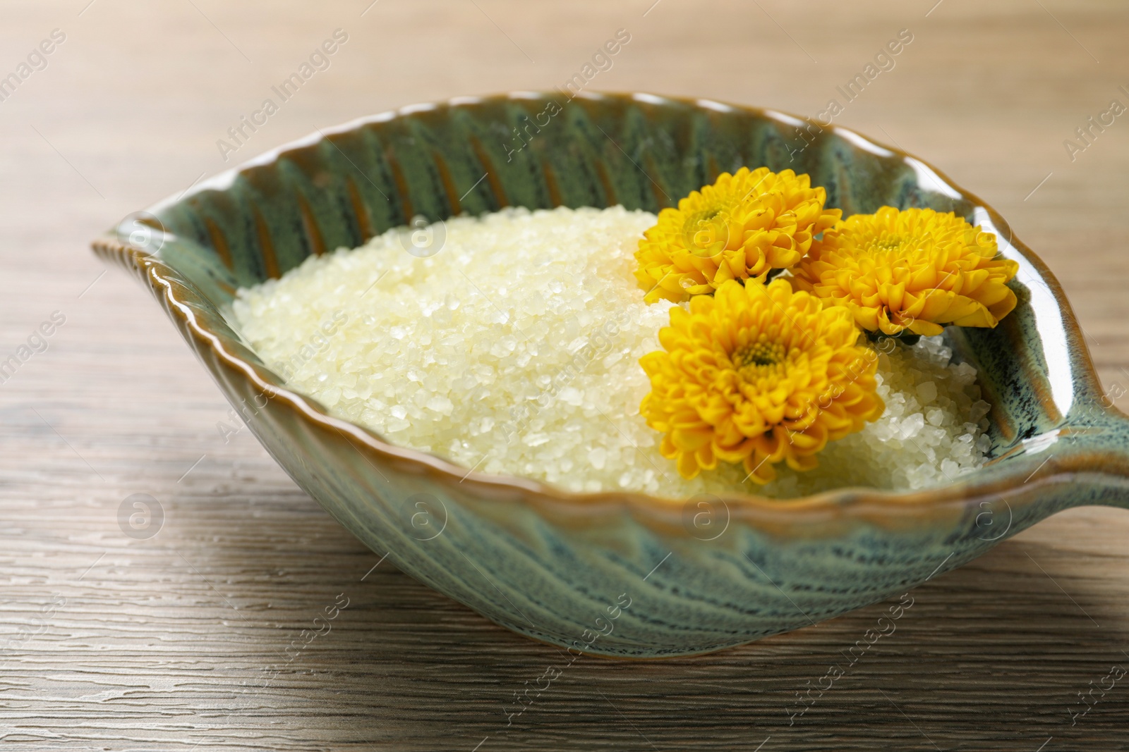 Photo of Bowl with natural sea salt and beautiful flowers on wooden table, closeup