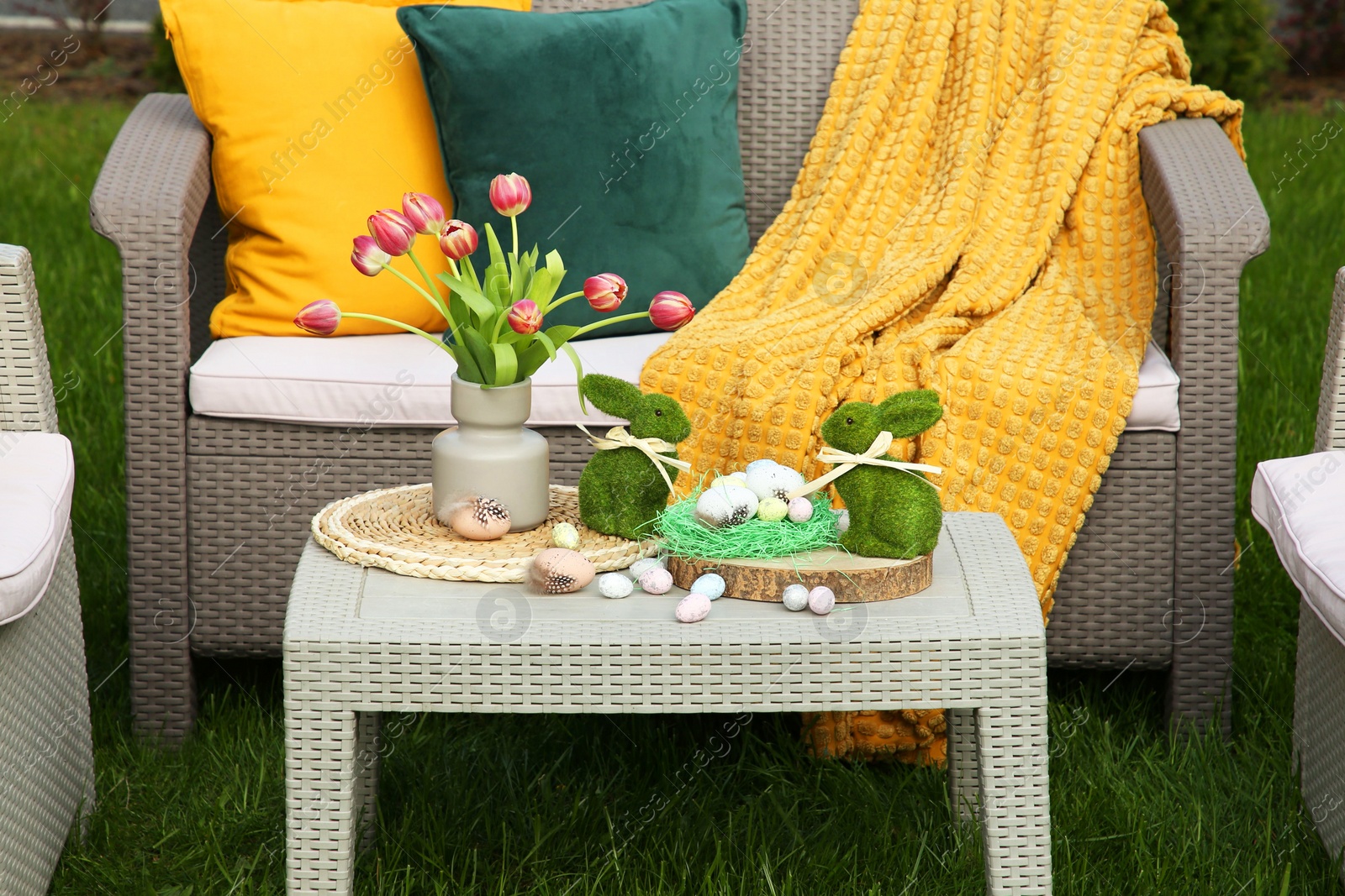 Photo of Easter decorations. Bouquet of tulips in vase, bunny figures and decorated eggs on table in backyard