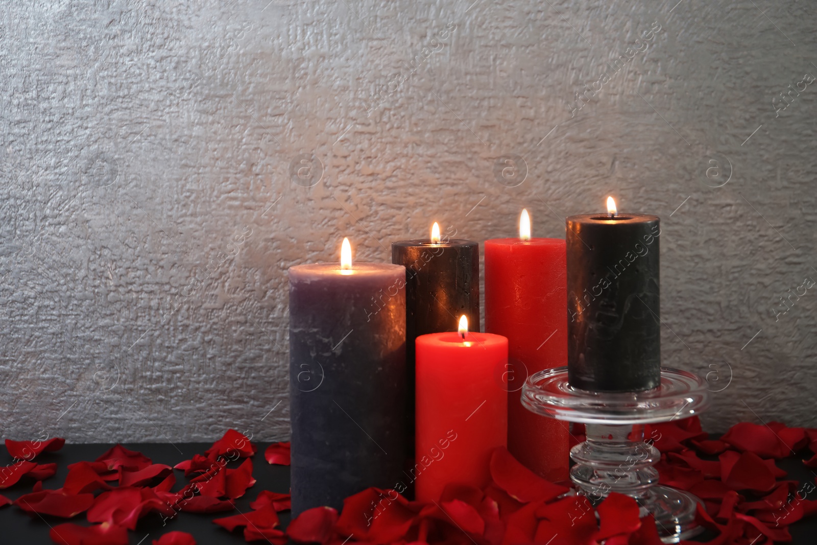 Photo of Candles with floral decor on table against color background