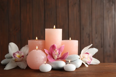 Photo of Beautiful composition with candles, flowers and stones on table against wooden background