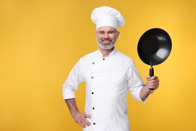 Photo of Happy chef in uniform with wok on orange background