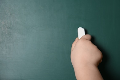 Photo of Little child writing on chalkboard, closeup. Space for text