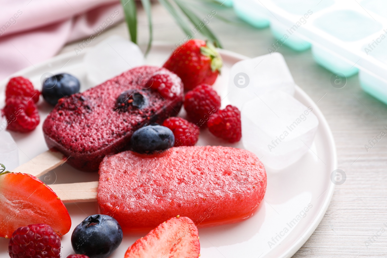 Photo of Plate of tasty berry ice pops on white wooden table, closeup. Fruit popsicle