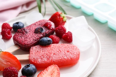 Plate of tasty berry ice pops on white wooden table, closeup. Fruit popsicle