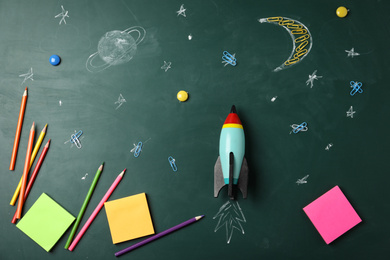 Bright toy rocket, school supplies and drawings on chalkboard, flat lay