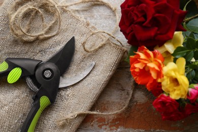 Photo of Secateur, beautiful roses and rope on table, flat lay