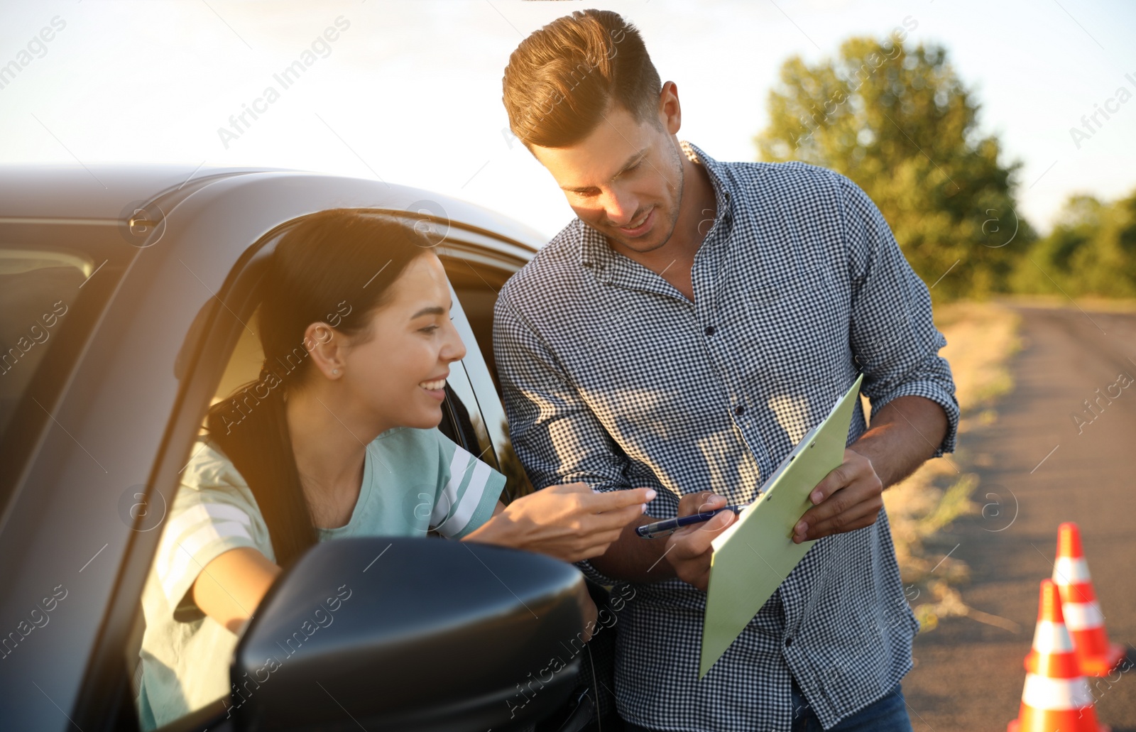 Photo of Instructor with clipboard near his student in car outdoors. Driving school exam