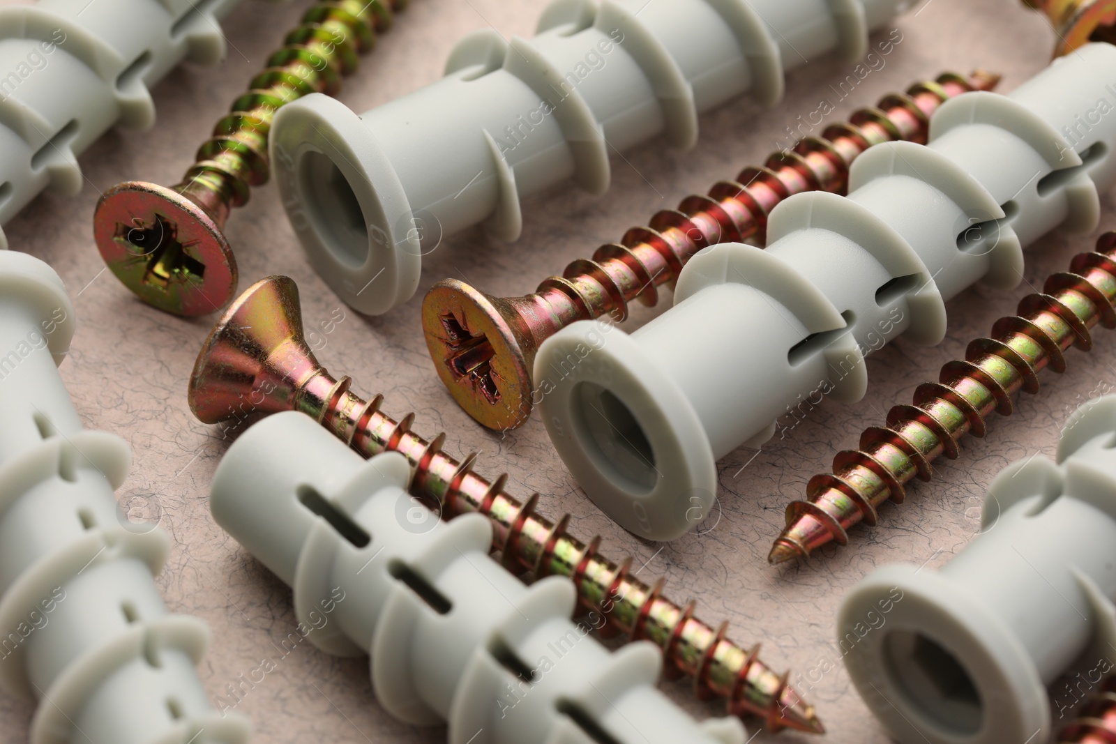 Photo of Many metal screws and dowels on beige table, closeup