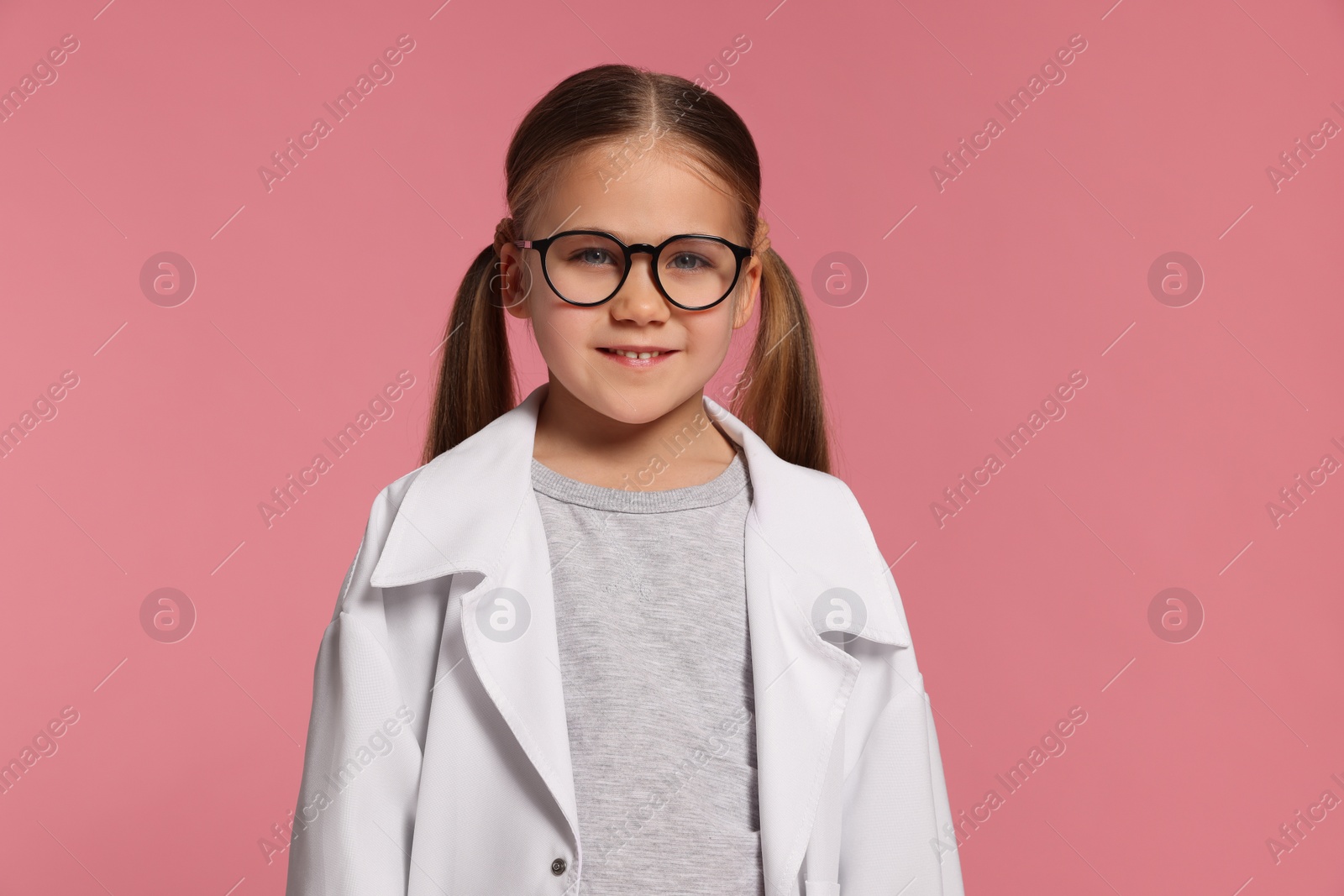 Photo of Portrait of little girl in medical uniform and glasses on pink background