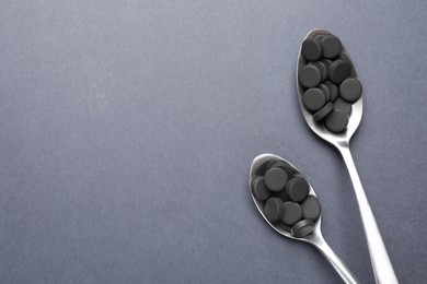 Photo of Activated charcoal pills in spoons on grey background, flat lay with space for text. Potent sorbent