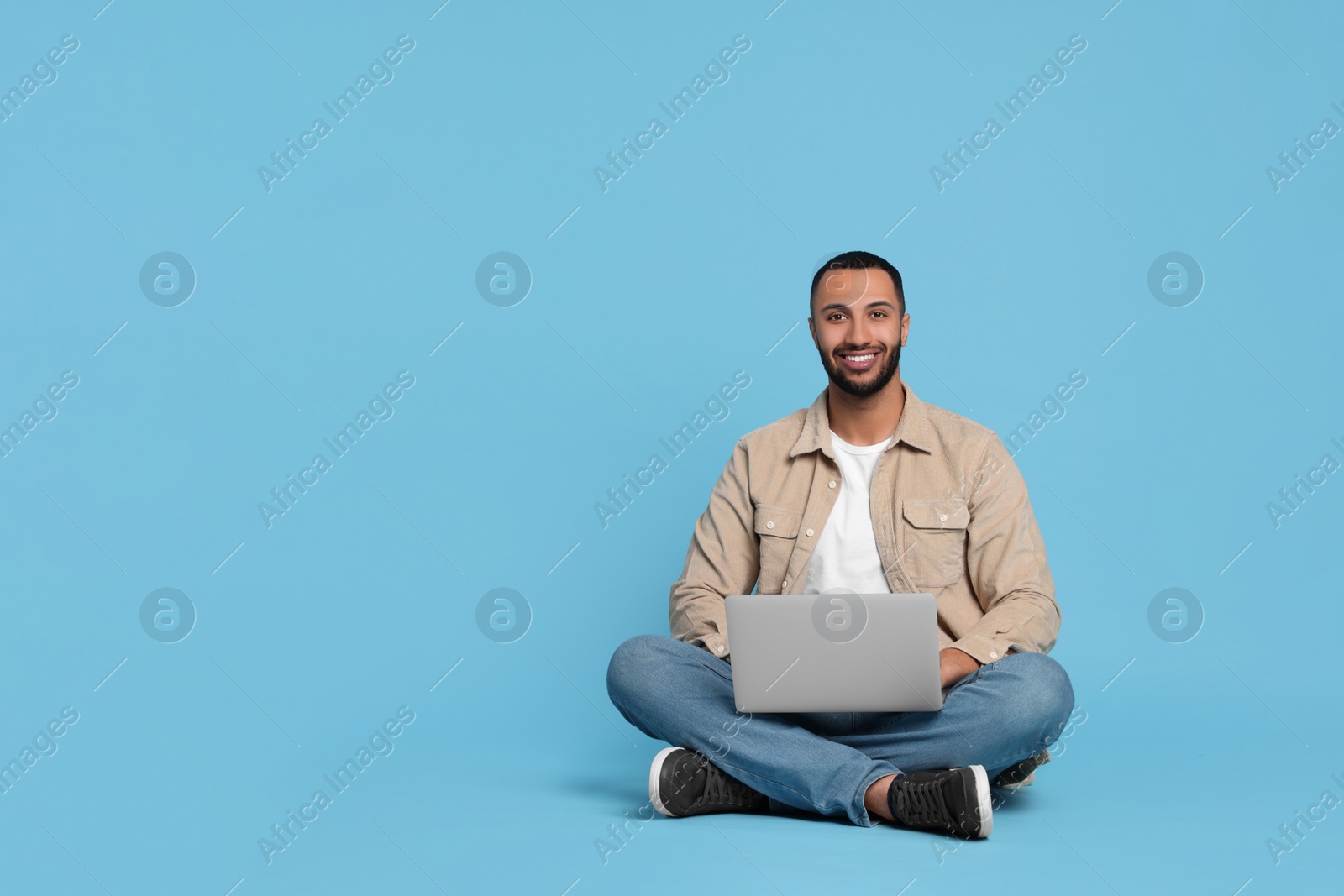 Photo of Smiling young man with laptop on light blue background, space for text