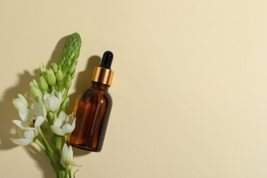 Photo of Bottle with cosmetic oil and flower on beige background, flat lay. Space for text