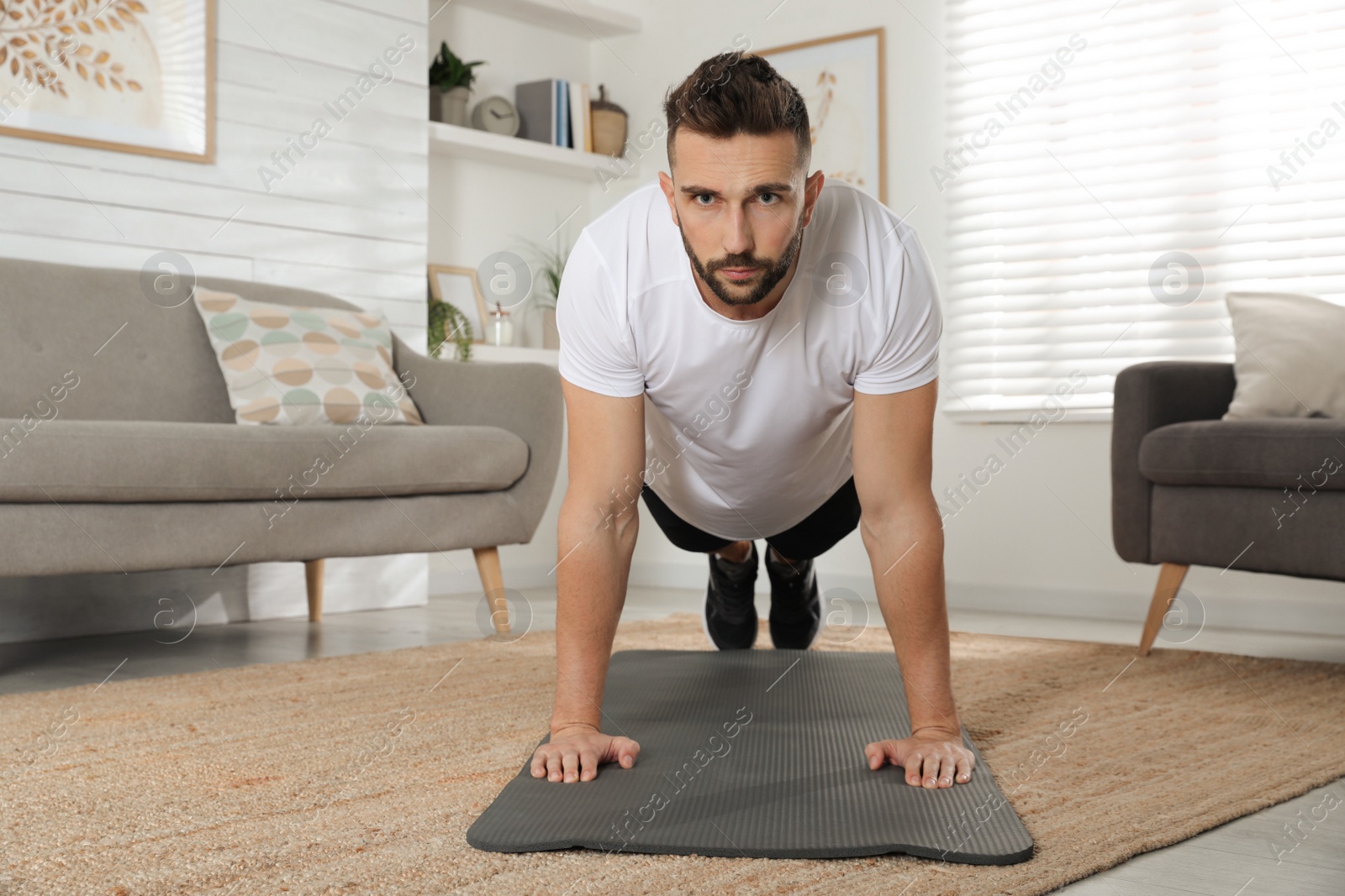 Photo of Handsome man doing plank exercise on yoga mat at home