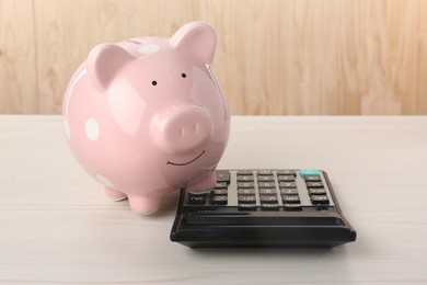 Calculator and piggy bank on light wooden table