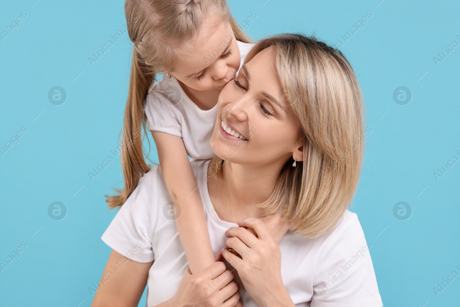 Photo of Daughter kissing her happy mother on light blue background