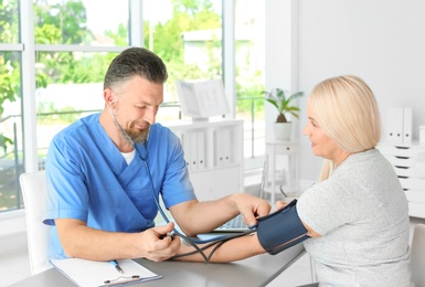 Male medical assistant measuring female patient blood pressure in clinic