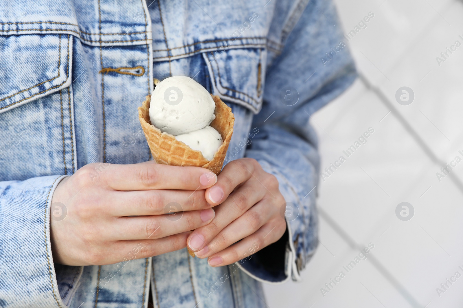 Photo of Woman holding delicious ice cream in waffle cone on light background, closeup