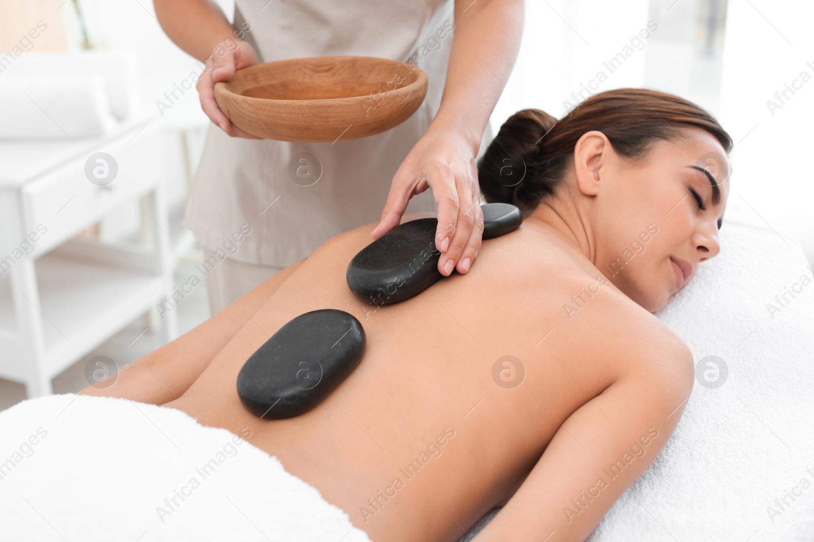 Photo of Beautiful young woman getting hot stone massage in spa salon