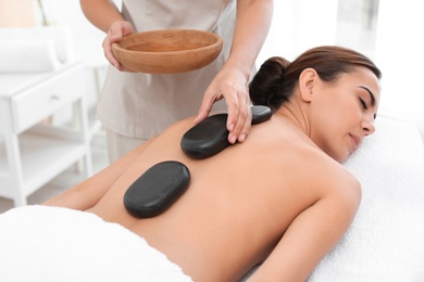 Photo of Beautiful young woman getting hot stone massage in spa salon