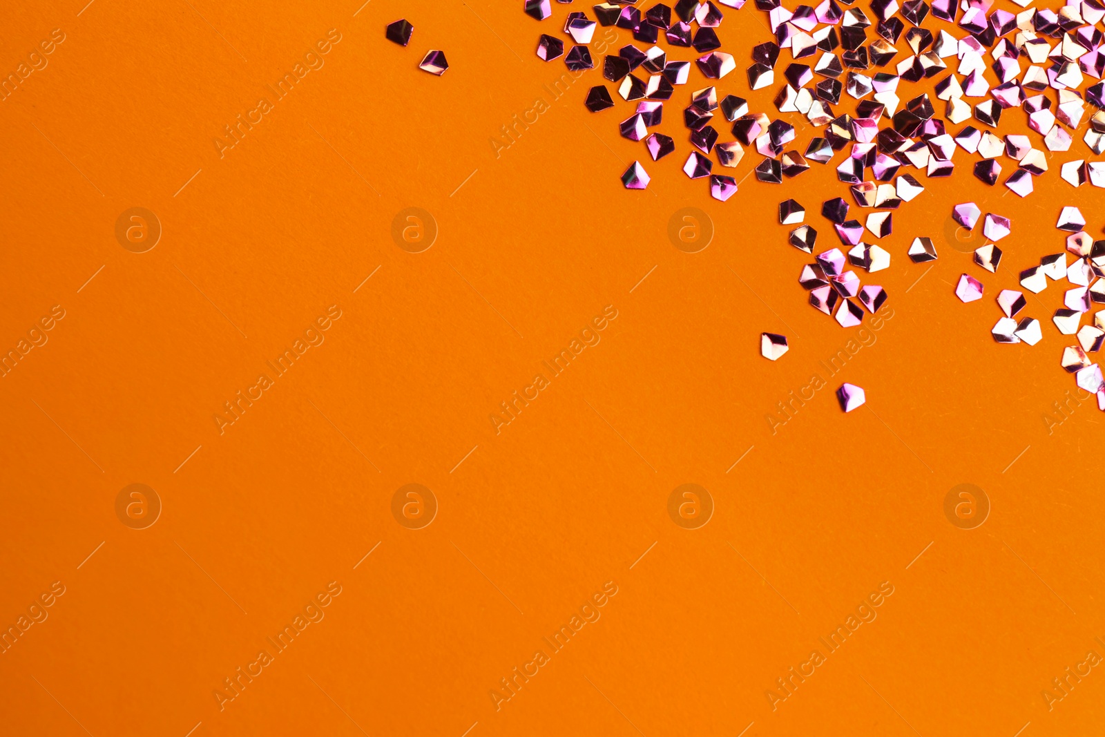 Photo of Shiny bright glitter on orange background, flat lay