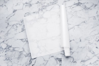 Photo of Roll of baking paper on white marble table, top view