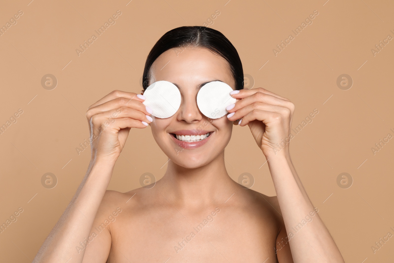 Photo of Young woman using cotton pads with micellar water on beige background
