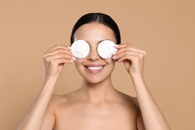 Young woman using cotton pads with micellar water on beige background